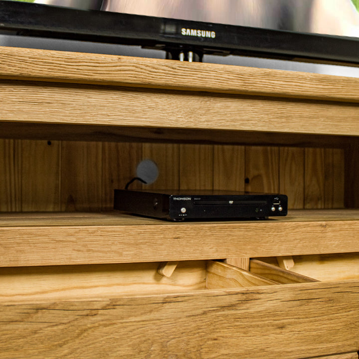 A closer view of the shelf on the Camden 2 Drawer White Oak Entertainment Unit, showing the cable hole in the back of the unit. There is a DVD player in the middle of the shelf.